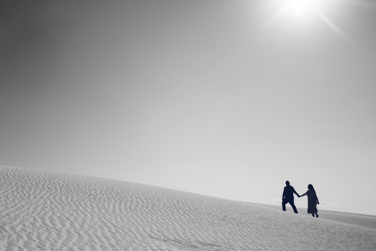 A couple walking across sunlit sand dunes