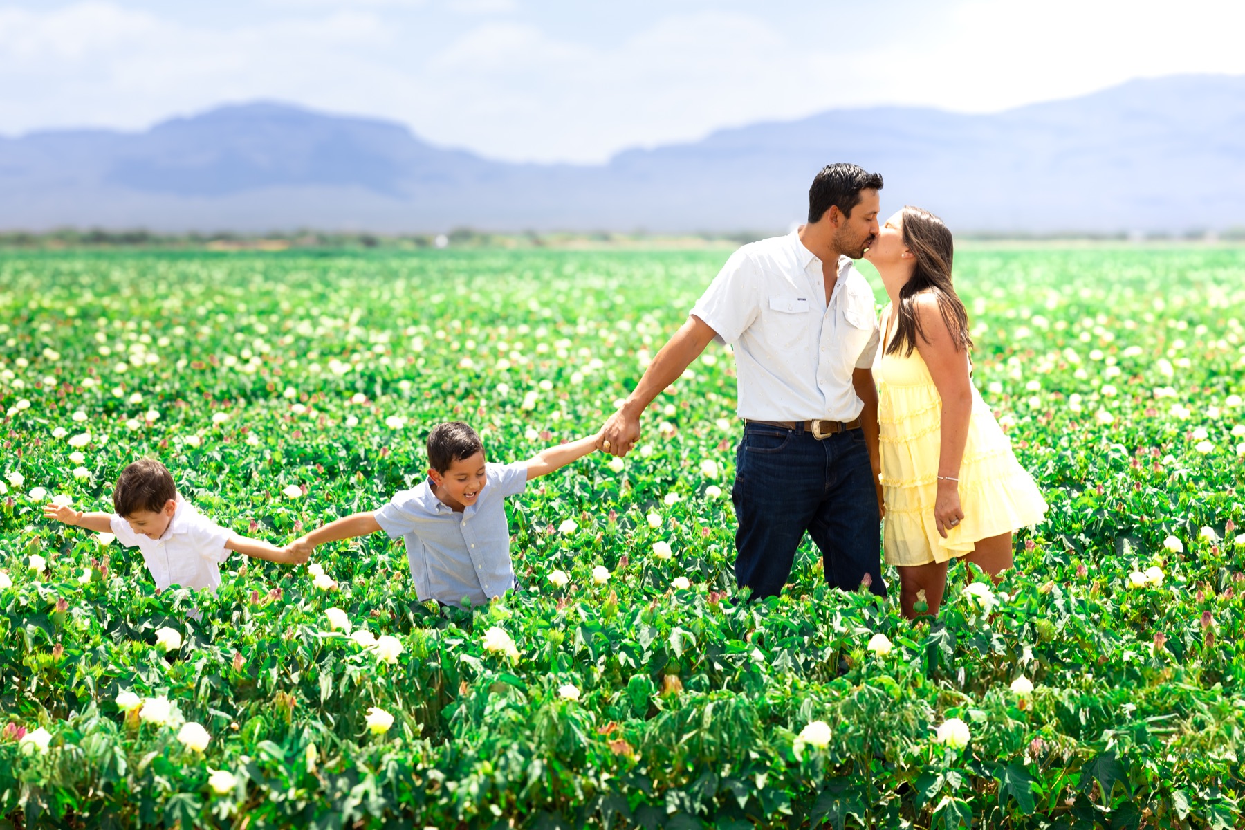 A family holding hands in a green field with mountains behind them