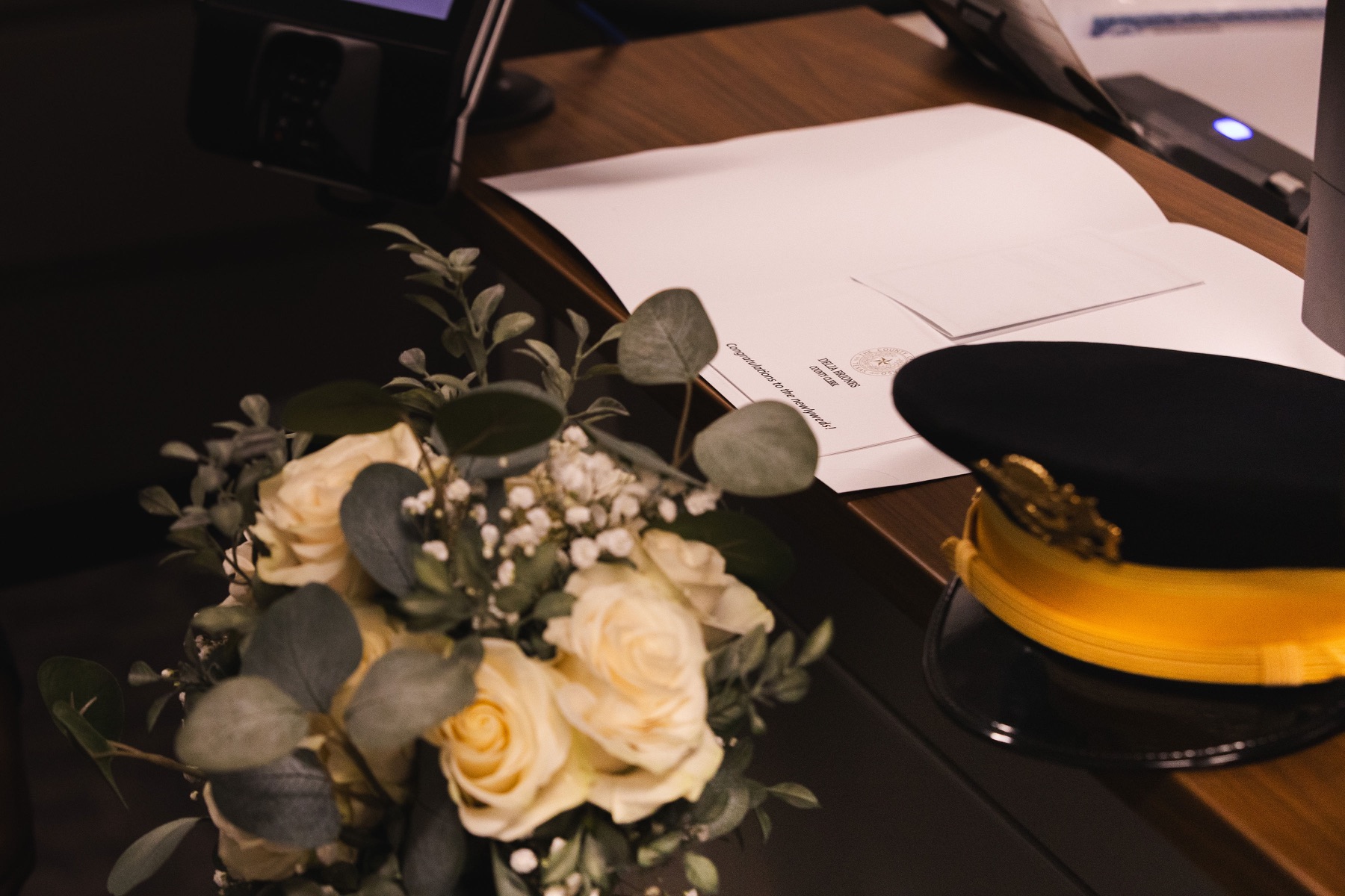 A wedding bouquet and military dress cap beside ceremony documents